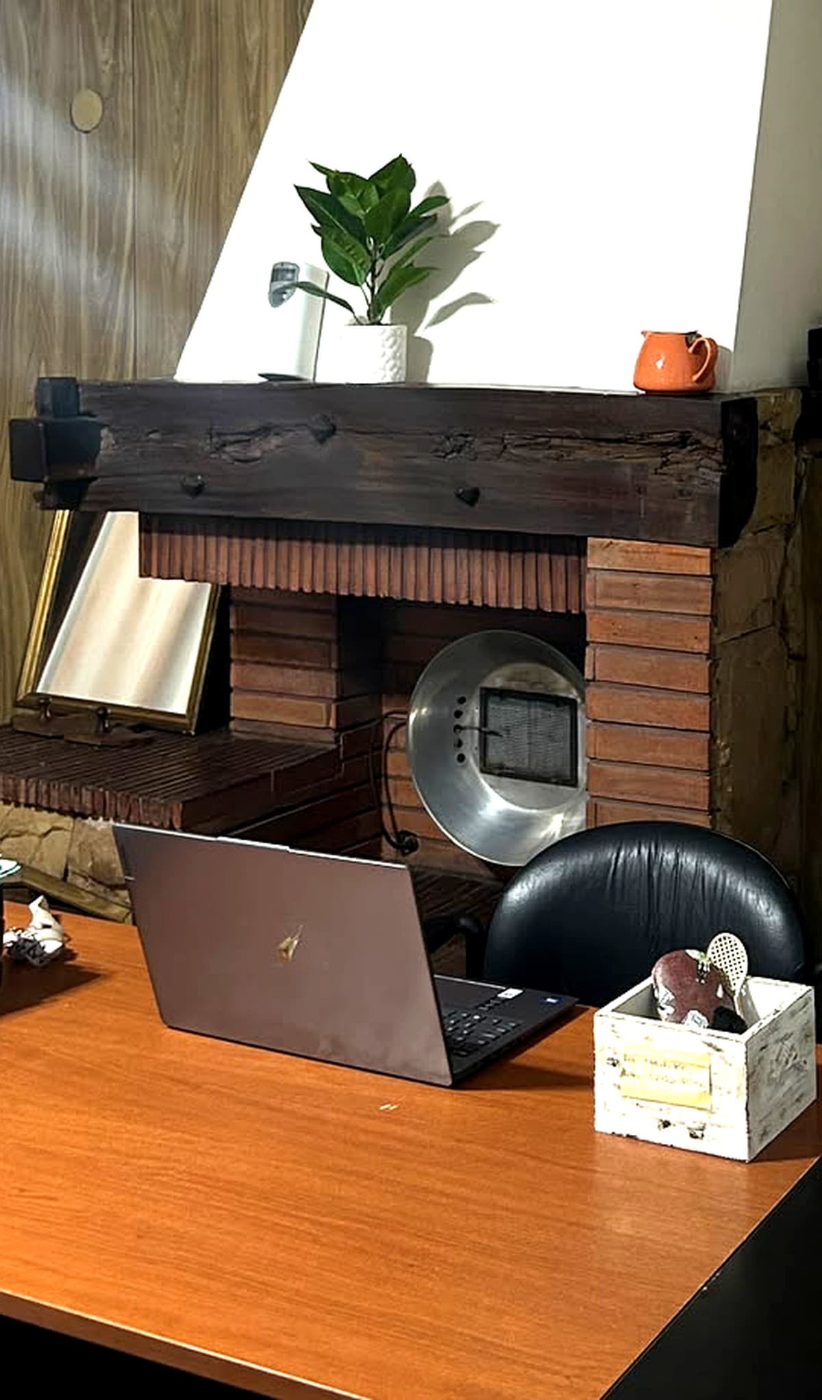 Escritorio de trabajo del estudio, con una notebook y el hogar de ladrillo detrás